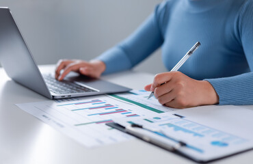 Businesswoman working in front of laptop at home office using pen and form for checking work on desk and analyzing business document. Finance concept.