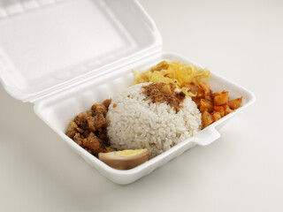 Steamed rice served with boiled egg, potato chip, fried tempeh in Styrofoam container