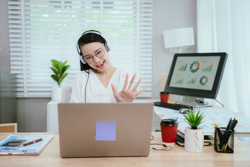 Smiling Asian female call center agent wearing a headset, speaking with a client at her office...