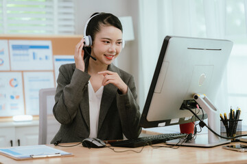 Smiling Asian female call center agent wearing a headset, speaking with a client at her office...