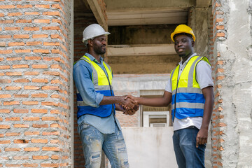 Engineers and construction workers wearing hard hats and reflective vests hold hands on a construction site, emphasizing the teamwork and cooperation that go into successful construction projects.