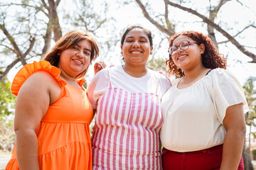 Obraz premium Three latin women embracing body positivity are smiling together in a park
