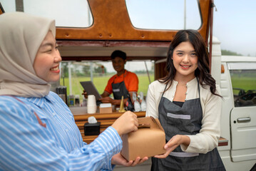 Indonesian southeast chinese asian female waiter serving food order to chinese muslim female customer. A small business on a truck