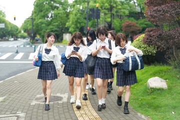In early June in Pudong, Shanghai, seven Japanese high school girls in summer uniforms walk together down a city street, smiling and chatting as they head to school under the soft morning sunlight.