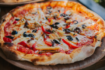 Pizza with cheese, vegetables and olives on a wooden stand. Delicious Italian cuisine. Vegetarian pizza close-up.