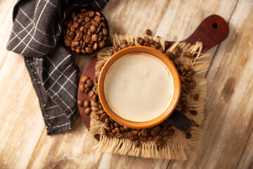 Flat white coffee in a black cup with coffee beans on rustic wooden table, french press on background.