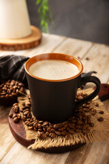 Flat white coffee in a black cup with coffee beans on rustic wooden table, french press on background.