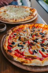 Pizza with cheese, vegetables and olives on a wooden stand. Delicious Italian cuisine. Vegetarian pizza close-up.