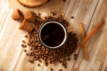Cafe de Olla. Traditional Mexican coffee and basic ingredients for its preparation, coffee, cinnamon and piloncillo, served in a metallic cup called "peltre" on a rustic wooden surface.