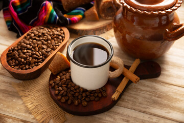 Cafe de Olla. Traditional Mexican coffee and basic ingredients for its preparation, coffee, cinnamon and piloncillo, served in a metallic cup called "peltre" on a rustic wooden surface.