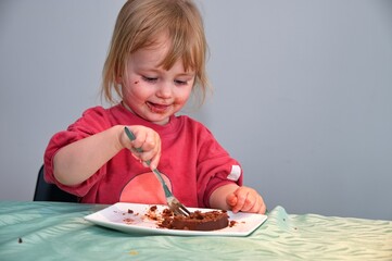 Little girl sitting at the table and eating chocolate cake