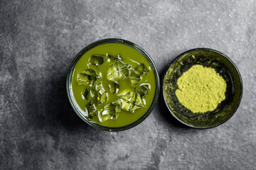 Closeup view of iced matcha green tea on the glass and matcha green tea powder in the bowl on the black table. Top view