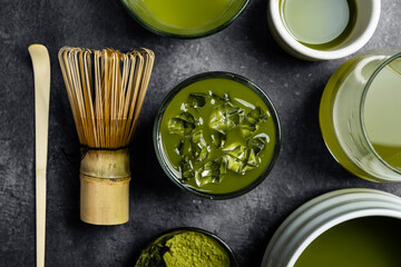 Closeup view of iced matcha green tea on the glass with a traditional bamboo brush whisk or chasen...