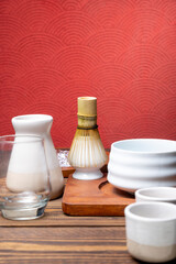 Traditional bamboo brush whisk or chasen with glass and bowl on wooden table. Accessories for making matcha green tea