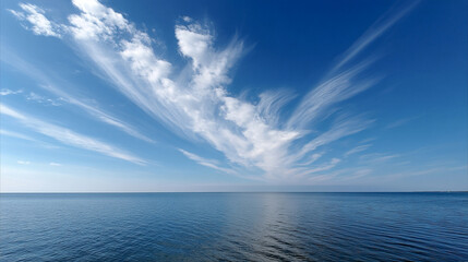 Delicate cirrus clouds stretch across blue sky above calm ocean water, creating peaceful atmosphere