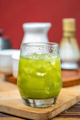 Closeup view of iced matcha green tea on the glass with a traditional bamboo brush whisk or chasen on wooden table. Accessories for making matcha green tea