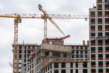Building development process: Cranes amidst buildings under construction against an overcast sky