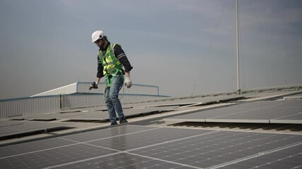 Blue collar worker is inspecting solar panel at rooftop of factory. Energy, sustainability.