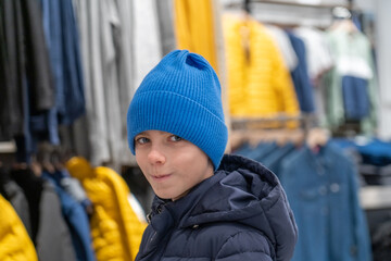 Portrait of a child in blue knit hat and puffer coat, ready for winter, shopping in store between...