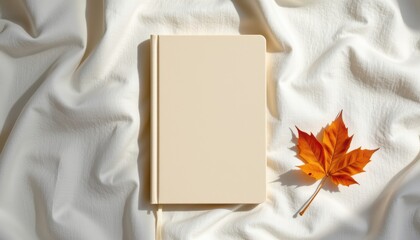 Fototapeta premium Minimalist Notebook with Blank Pages and a Vibrant Autumn Maple Leaf on Soft White Fabric