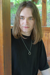 Young man with long hair gazing thoughtfully in a wooden cabin