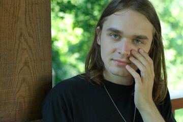 Young man with long hair contemplates in a serene garden setting