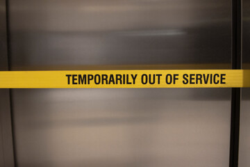 A yellow banner warning an elevator is out of service. The elevator is stainless brushed steel © F Armstrong Photo
