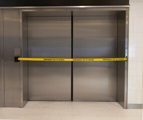 A yellow banner warning an elevator is out of service. The elevator is stainless brushed steel © F Armstrong Photo