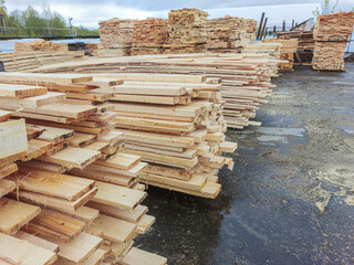 Boards and lumber are stacked in the open air.