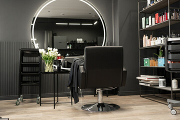 Modern hair salon interior with stylish black chair and circular mirror