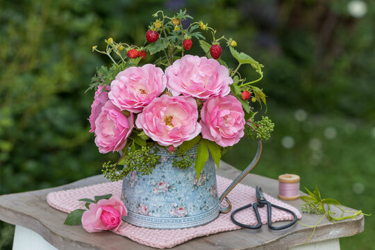 Blumenstrau&szlig; mit pink Rosen, Walderdbeeren und Wildem Wein im vintage Krug im Garten