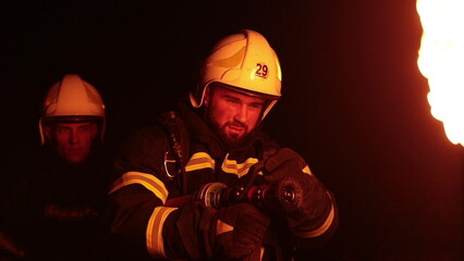 Brave firefighters battling intense flames at night. Firelight illuminates their determined faces as they work courageously in darkness. Dramatic scene of rescue, danger, and heroism.