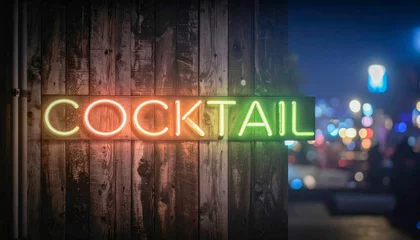 A neon sign that says Cocktail on it. The sign is lit up and is on a wooden post