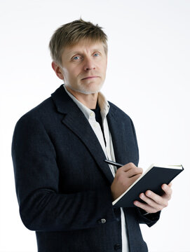 A serious and intelligent man holding a notebook and pen, evoking creativity and contemplation against a clean white backdrop.