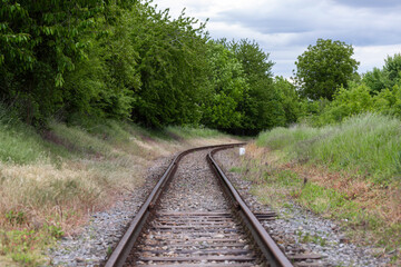 Curving train tracks surrounded by green meadow and dense foliage, blending industry with...