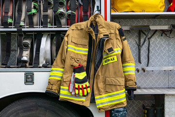 firefighter's jacket with reflective stripes and gloves hanging on a fire truck next to a compartment with rescue equipment. The label "STRAŻ" indicates the Polish fire service © Adam