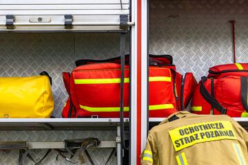Equipment of a volunteer fire department stored in a fire truck compartment – visible red and yellow rescue bags and a firefighter’s jacket labeled “Ochotnicza Straż Pożarna” (Volunteer Fire Departmen © Adam