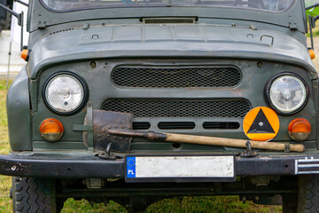 vintage UAZ military off-road vehicle, with a shovel mounted on the bumper and a civil defense sign. The vehicle is displayed during a historical or military event. © Adam