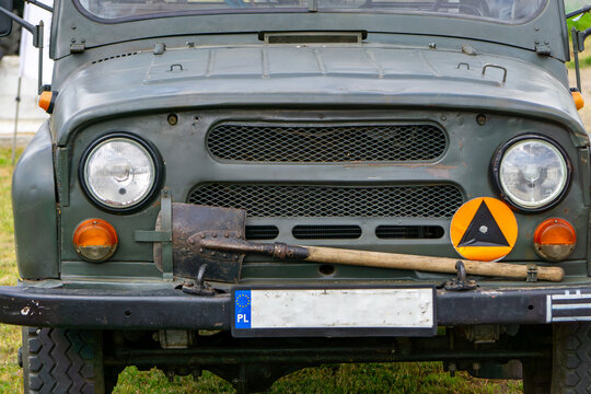 vintage UAZ military off-road vehicle, with a shovel mounted on the bumper and a civil defense sign. The vehicle is displayed during a historical or military event. - Powered by Adobe