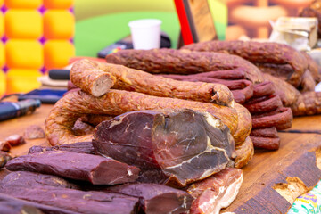 Traditional cured meats displayed on a wooden board at a fair. Slices of dried sausage and aged ham prepared for tasting