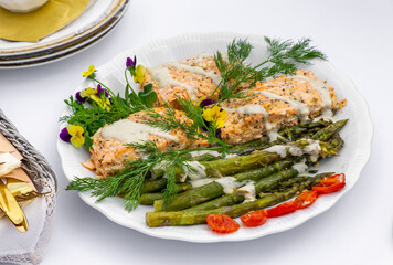 Salmon fillet served with grilled green asparagus, drizzled with sauce and garnished with fresh dill and edible flowers. Elegantly presented dish on a white plate, perfect for a festive meal.