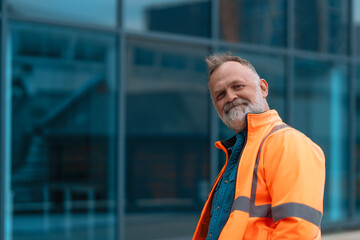 Man dressed in bright orange safety gear outfit stands near modern office building