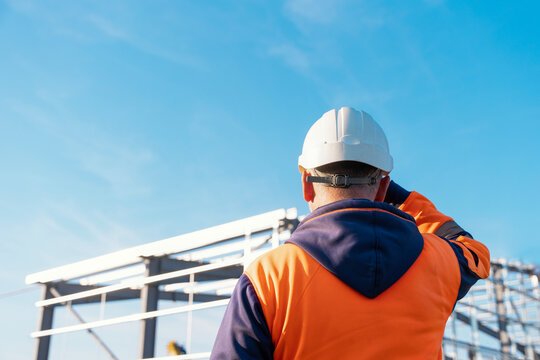 Builder watching construction process of new industrial building warehouse structure made of steel frame