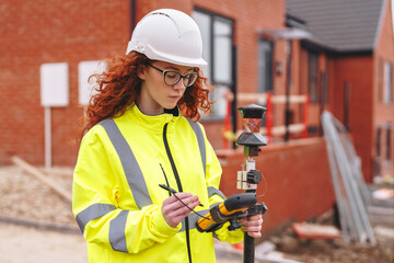 Portrait of confident female land surveyor with long hair in bright safety gear using surveying...