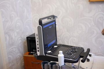 An ultrasound machine with a screen, keyboard, and a bottle of gel is positioned in a clinical setting, ready for diagnostic imaging.