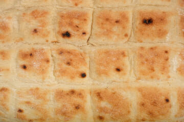 A close-up shot of the surface of a flatbread with golden-brown baked spots and a textured square pattern