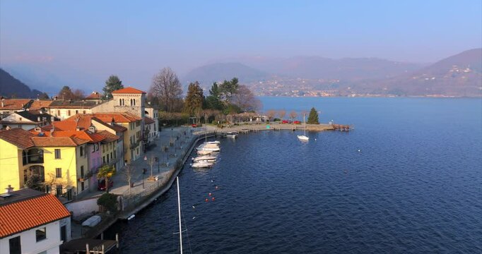 Pella village waterfront on Lake Orta, colorful buildings, moored boats, hazy mountains, Italian lakes travel, Italy. Aerial drone pov