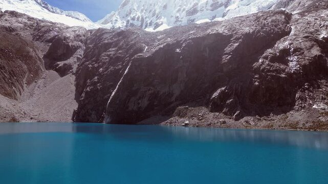 Low flight across vivid blue mountain lake toward cliff below mtn peak