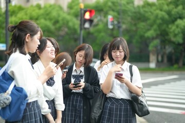 In early June, in Pudong, Shanghai, seven Japanese high school girls dressed in summer uniforms are standing at a crosswalk on a city street, laughing and chatting together on their way to school.