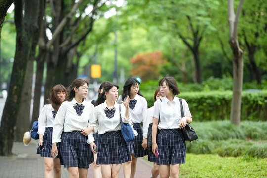 In early June in Pudong, Shanghai, seven Japanese high school girls wearing summer uniforms are walking to school along a lush green street, surrounded by vibrant foliage and early summer sunlight.